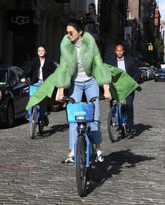 a woman riding on the back of a blue bike down a cobblestone street