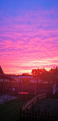 the sky is pink and purple as the sun sets over a park area with benches