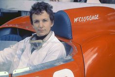 a woman sitting in the driver's seat of an old race car, looking at the camera