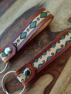 two leather keychains with metal rings on top of a wooden table next to each other