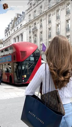 a woman carrying a louis vuitton bag in front of a double decker bus