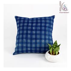 a blue and white plaid pillow sitting next to a potted plant