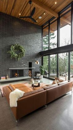 a living room with large windows and a couch in front of a fire place that has a potted plant on top of it