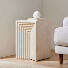 a white vase sitting on top of a wooden box next to a chair and ottoman