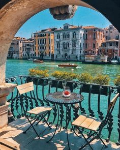 an outdoor table and chairs on a balcony overlooking a canal with boats in the water