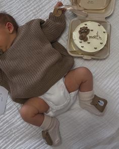 a baby laying on a bed next to a cake and other items in a suitcase