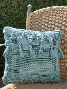 a blue crocheted pillow sitting on top of a chair next to a wicker chair