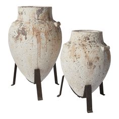 two white vases sitting next to each other on metal legs with rusted paint