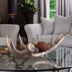 a glass coffee table with antlers on it in front of white couches and windows