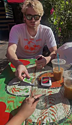 two people sitting at an outdoor table with drinks and cell phones in front of them