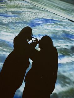 two people standing next to each other in front of a large screen with water on it