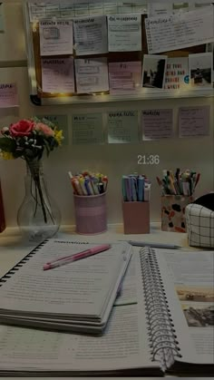 an open book sitting on top of a desk next to a vase filled with flowers