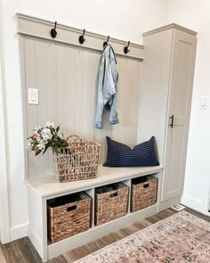 a white bench with baskets on it next to a rug and coat rack filled with clothes