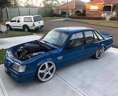 a blue car parked in front of a house with the hood up and an engine bay open