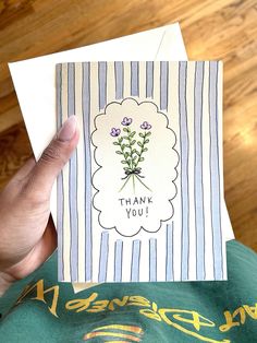 a person holding up a thank you card with flowers in the center and an envelope that says, thank you