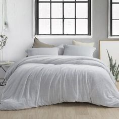 a bed with white linens and pillows in a room next to two large windows