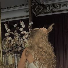 a woman brushing her hair in front of a mirror with flowers on the wall behind it