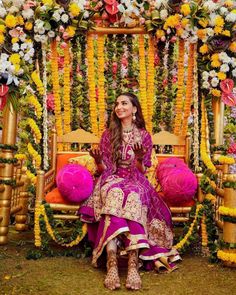 a woman sitting on top of a wooden bench covered in flowers and garlanded with lights