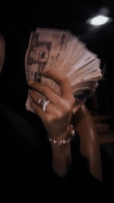 a woman holding up a stack of cash in her hand with the light shining on her face