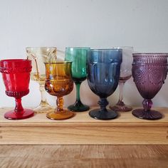 several different colored wine glasses lined up on a wooden table with white wall in the background