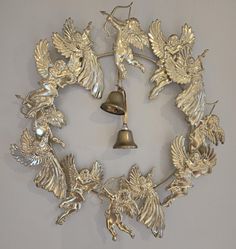 a silver clock with angels on it and a bell hanging from the front, surrounded by other metal objects