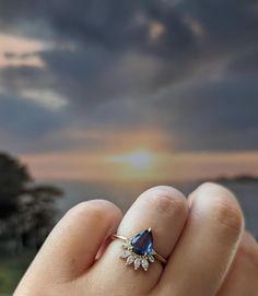 a woman's hand holding a ring with a blue tear shaped stone on it