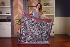 a woman holding up a purple and black blanket on top of a hard wood floor