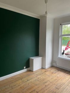 an empty room with green painted walls and wood flooring on the far wall is a white radiator