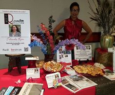 a woman standing next to a table full of food and magazines with flowers in vases