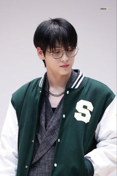 the young man is wearing glasses and a green varsity jacket with white lettering on it