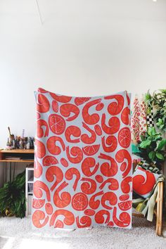 a large red and white blanket sitting on top of a floor next to a potted plant