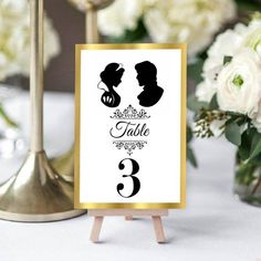 the table numbers are displayed on easers with white flowers in vases behind them