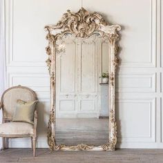 an ornate gold framed mirror sitting on top of a wooden floor next to a chair