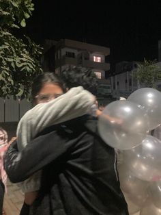 two people hugging each other with white balloons