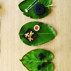 three green leaf shaped dishes on top of a wooden table with chopsticks and utensils