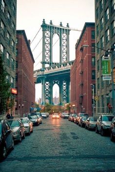 cars are parked on the street in front of tall buildings with a bridge above them