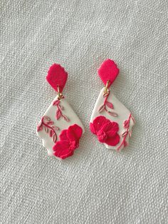 two pairs of pink and white flower earrings on top of a cloth covered tablecloth