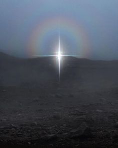 a cross in the middle of a foggy field with a bright light coming from behind it