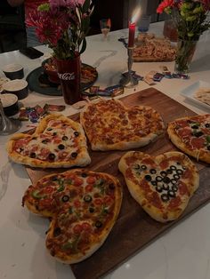 heart shaped pizzas on a wooden cutting board with candles and flowers in the background