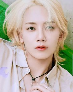 a young man with blonde hair wearing a collared shirt and necklace, posing for the camera