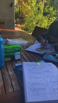 a person sitting at a table writing on a piece of paper next to a blue water bottle