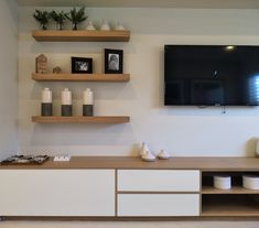 a flat screen tv mounted to the wall above a wooden shelf with bowls and cups on it