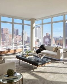 a living room filled with furniture and large windows overlooking the cityscape in the distance