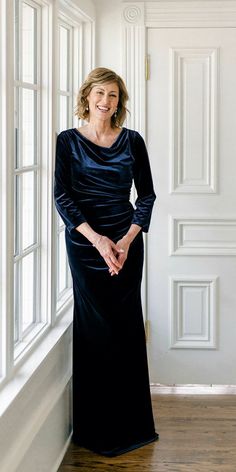 a woman standing in front of a window wearing a black dress and smiling at the camera