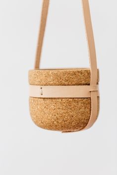 a cork bag hanging from a hook on a white wall with a tan leather strap