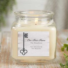 a candle with a label on it sitting on a table next to some flowers and greenery