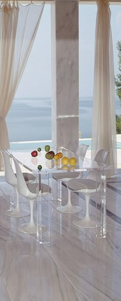 a dining table with chairs and fruit on it in front of a window overlooking the ocean