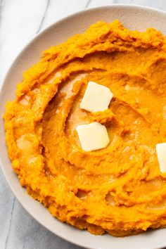 a white bowl filled with mashed sweet potatoes and topped with butter cubed cheese