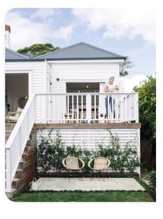 two chairs sitting on top of a wooden deck next to a white house with stairs