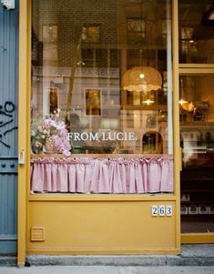 a storefront with pink curtains and flowers in the window